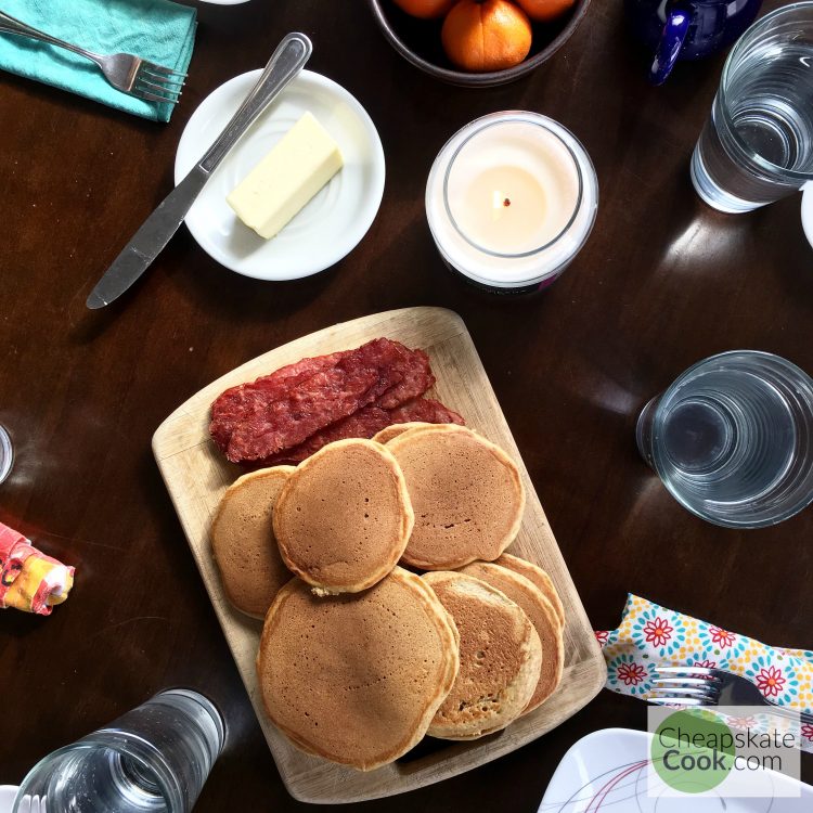 weekend breakfast table with pancakes, bacon, and oranges.