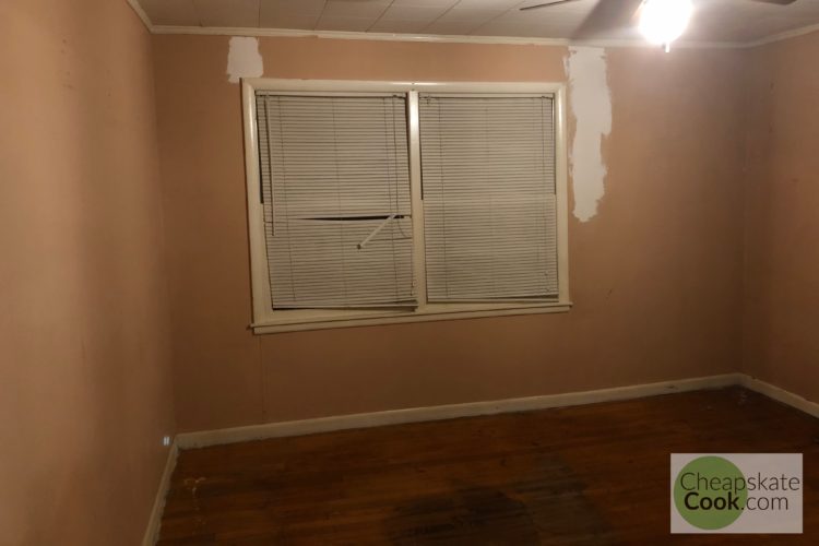 room with peach colored walls, broken blinds and patched drywall