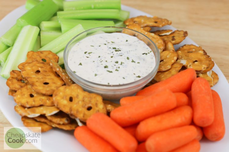 Ranch dip in a bowl surrounded by celery, carrots, and pretzels